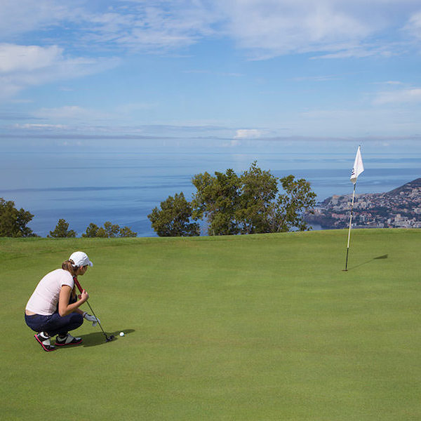 Woman golfer putting on Palheiro Golf, Madeira, with view to the sea